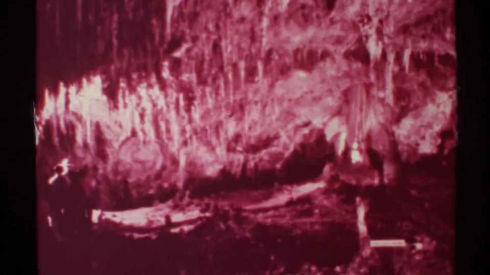 1972 New Mexico 8mm frame of a pink cave interior with clustered rock formations, dark foreground shadows, and visible film-edge wear.