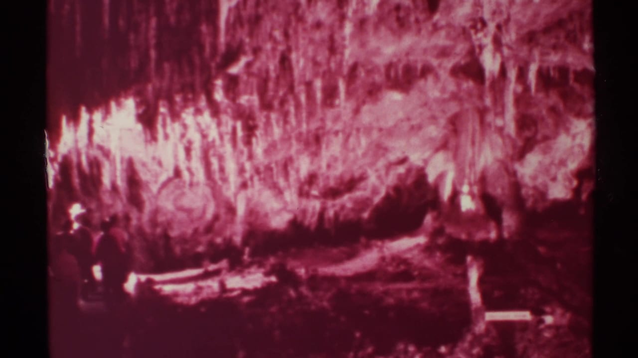 1972 New Mexico 8mm frame showing a red-tinted cavern wall, stalactite-like formations, and small visitors near the lower left.