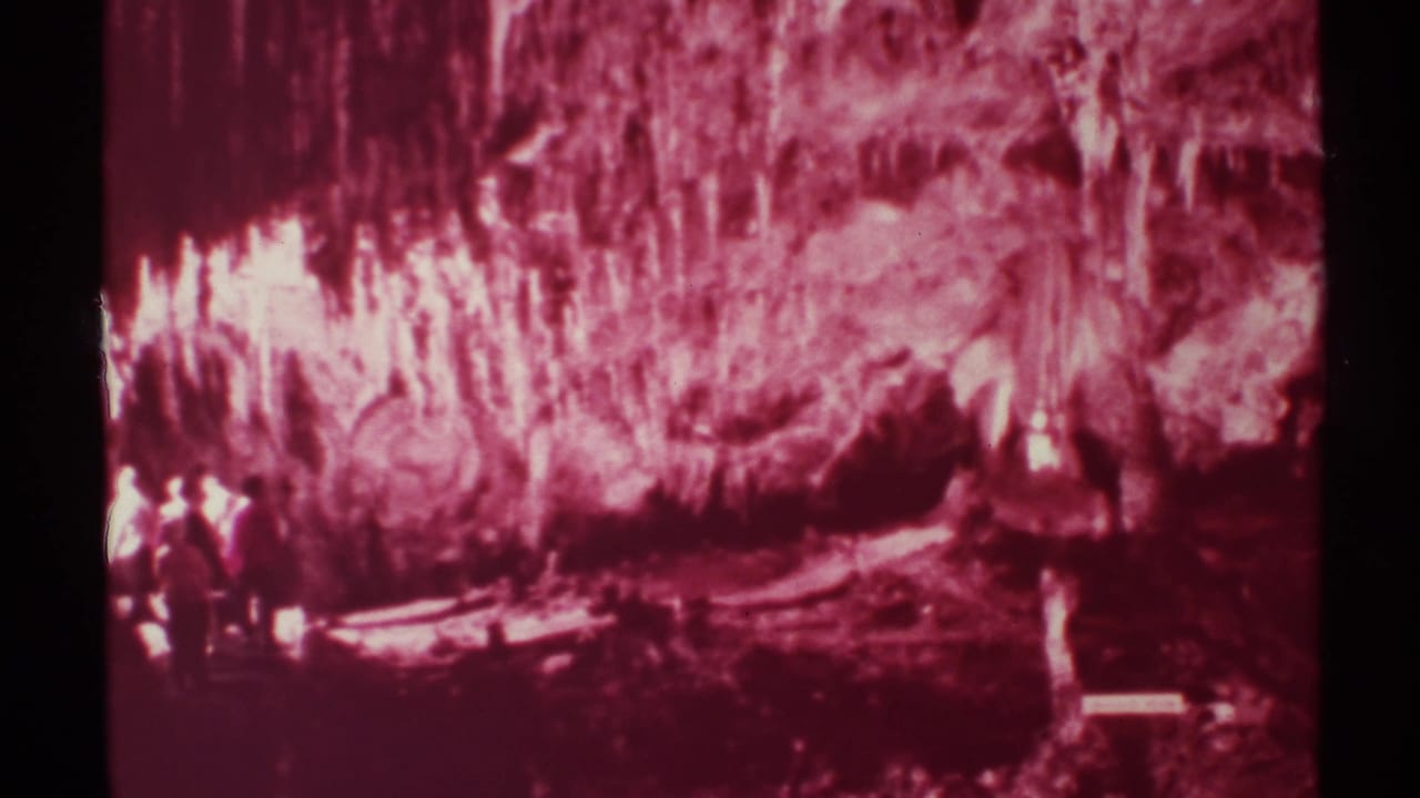 Red cave chamber with textured formations and visitors gathered near the lower left.