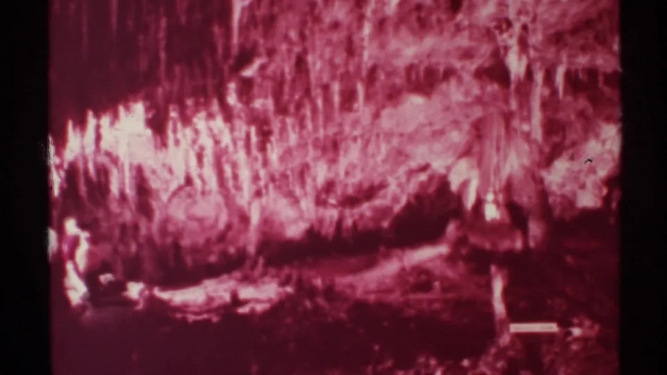 1972 New Mexico 8mm frame showing visitors at the lower left beneath bright red cave formations and heavy shadow.