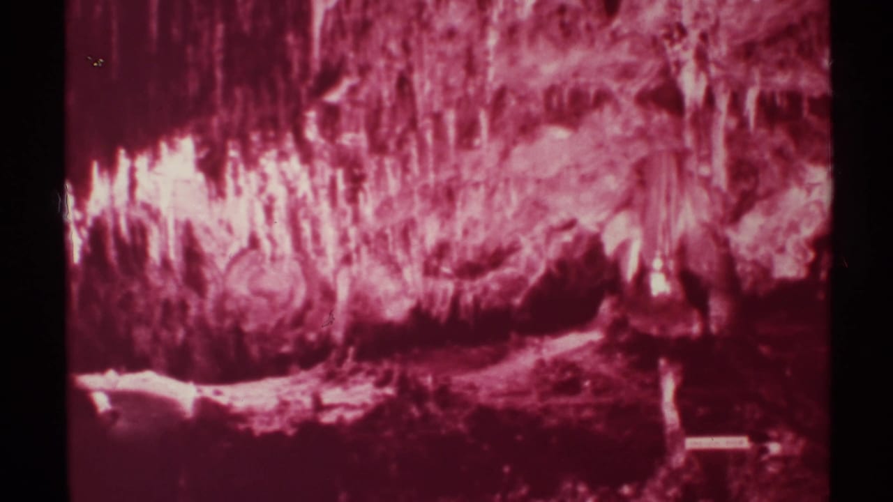 Red-lit cave formations fill the frame with dark film borders and no clear people visible.