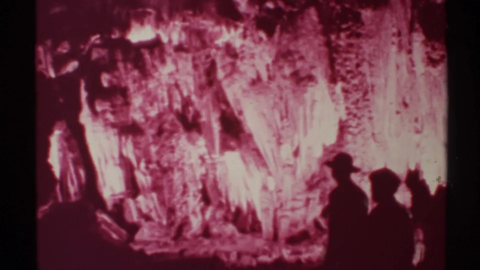 Silhouetted figures in 1972 New Mexico cave footage stand near glowing red and white stalactite formations.