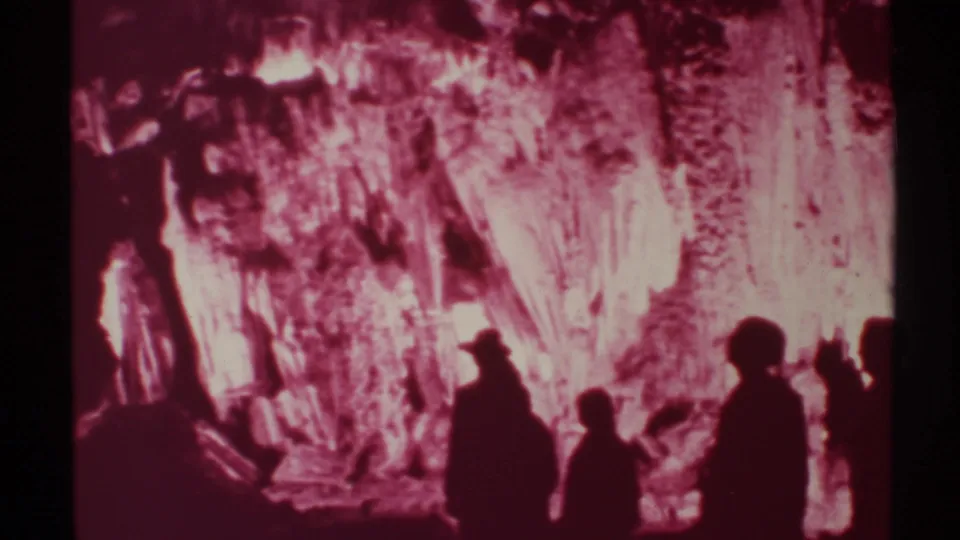 A group of silhouetted visitors appears in 1972 New Mexico cave footage, facing bright stalactites and textured rock.