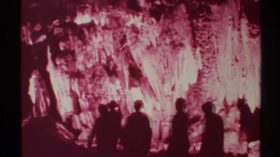 In a 1972 New Mexico cavern scene, multiple visitors are silhouetted against bright red-lit stalactites and rock textures.