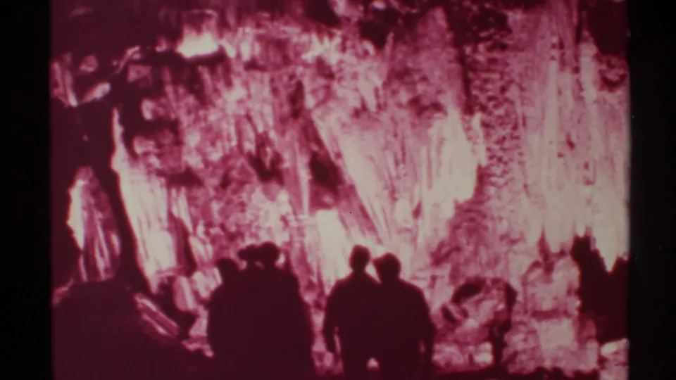 1972 New Mexico 8mm frame of visitors silhouetted against a pink-red illuminated cavern wall and formations.