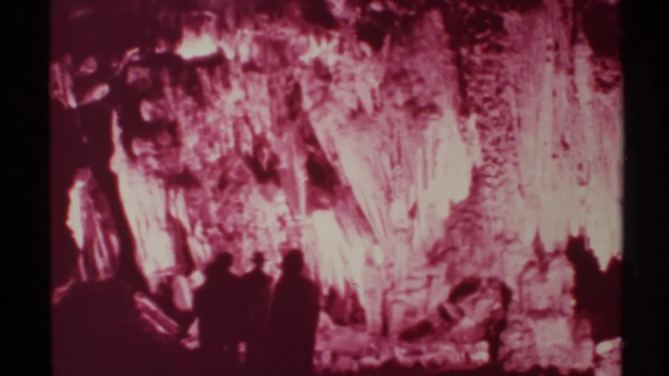 1972 New Mexico home-movie frame showing a small visitor group walking through a pink-lit cavern interior.