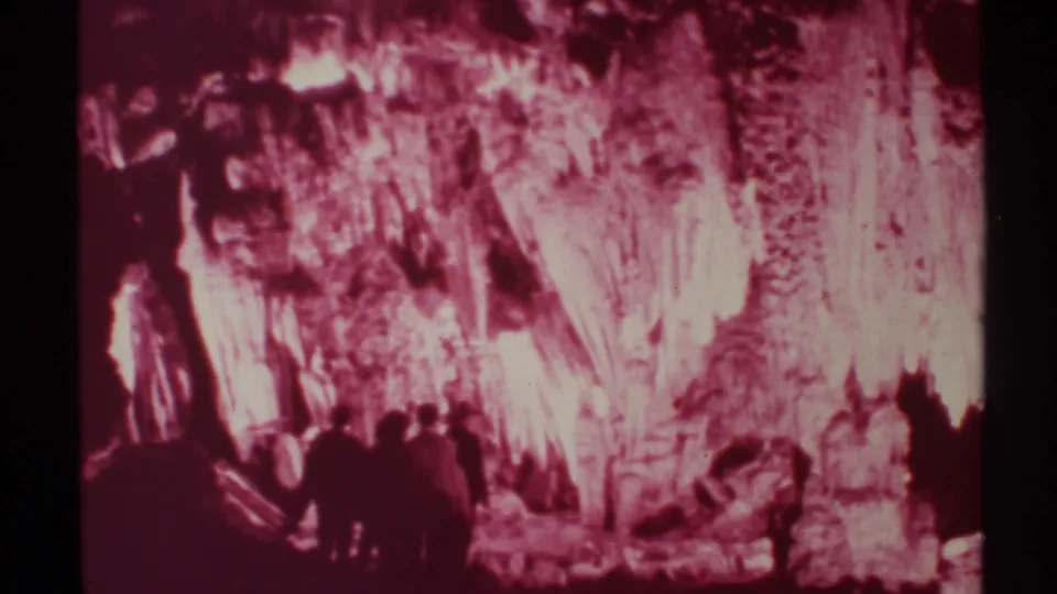 1972 New Mexico 8mm frame with several visitors clustered below pink-red illuminated cave formations.