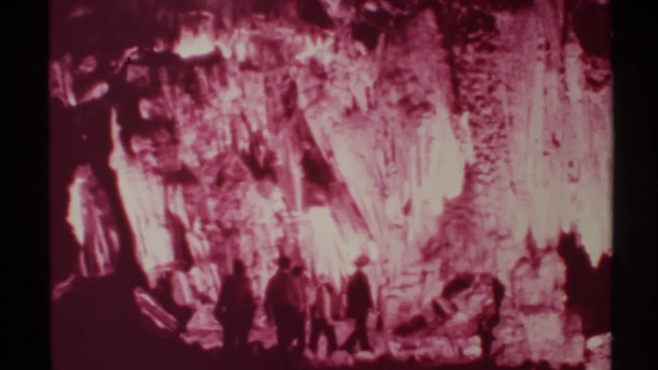 1972 New Mexico home-movie frame of silhouetted visitors under a glowing pink cavern wall and rock formations.