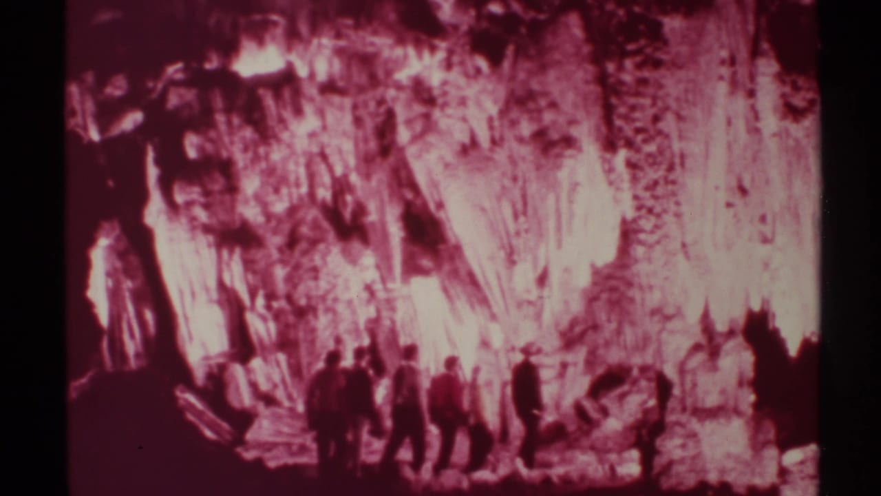 In 1972 New Mexico footage, several men appear as dark silhouettes against red-lit cave formations and shadowed rock walls.