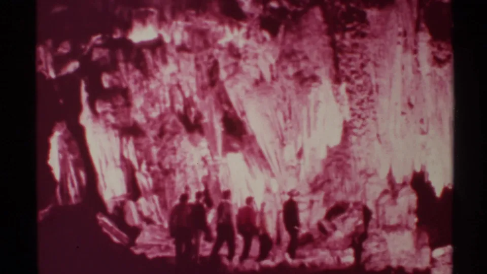 In 1972 New Mexico footage, several men appear as dark silhouettes against red-lit cave formations and shadowed rock walls.