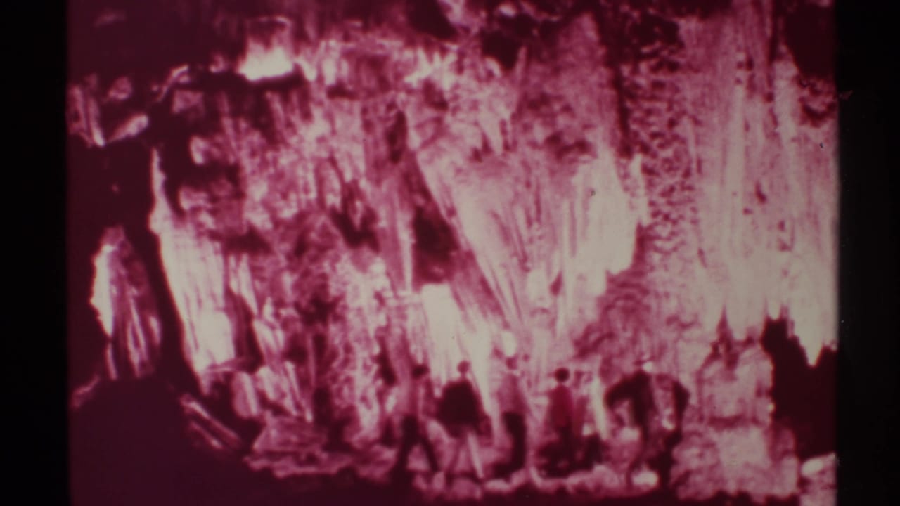 A group of men moves across a red-lit cavern with bright rock formations in the background.
