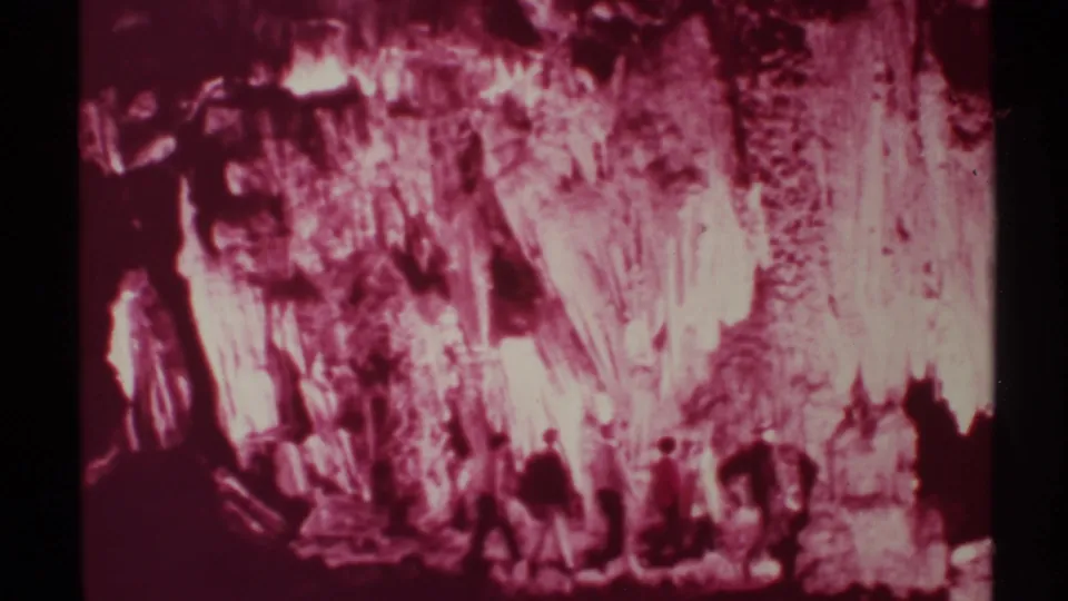 The group continues through the New Mexico cave, their figures blurred by motion against bright red and pink rock surfaces.