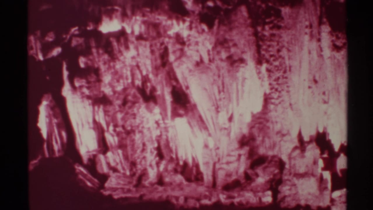 Cavern wall with bright mineral formations and dark figures at the lower right.