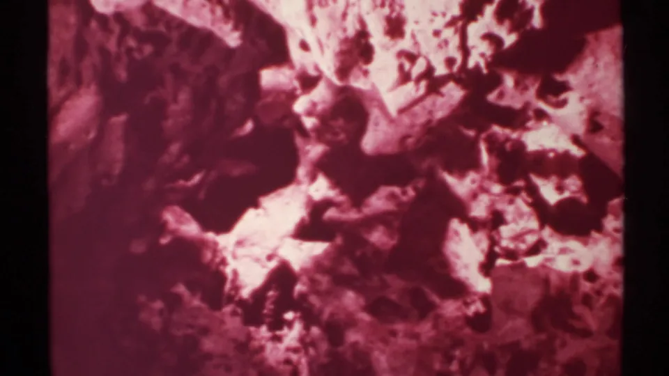 1972 New Mexico 8mm frame showing a tight, magenta-toned view of rugged rock texture and shadowed cracks.