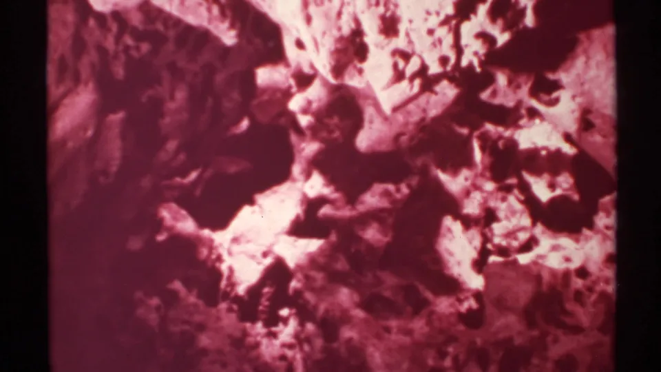 1972 New Mexico 8mm frame of textured rock filling the view, with magenta aging color and black frame border visible.