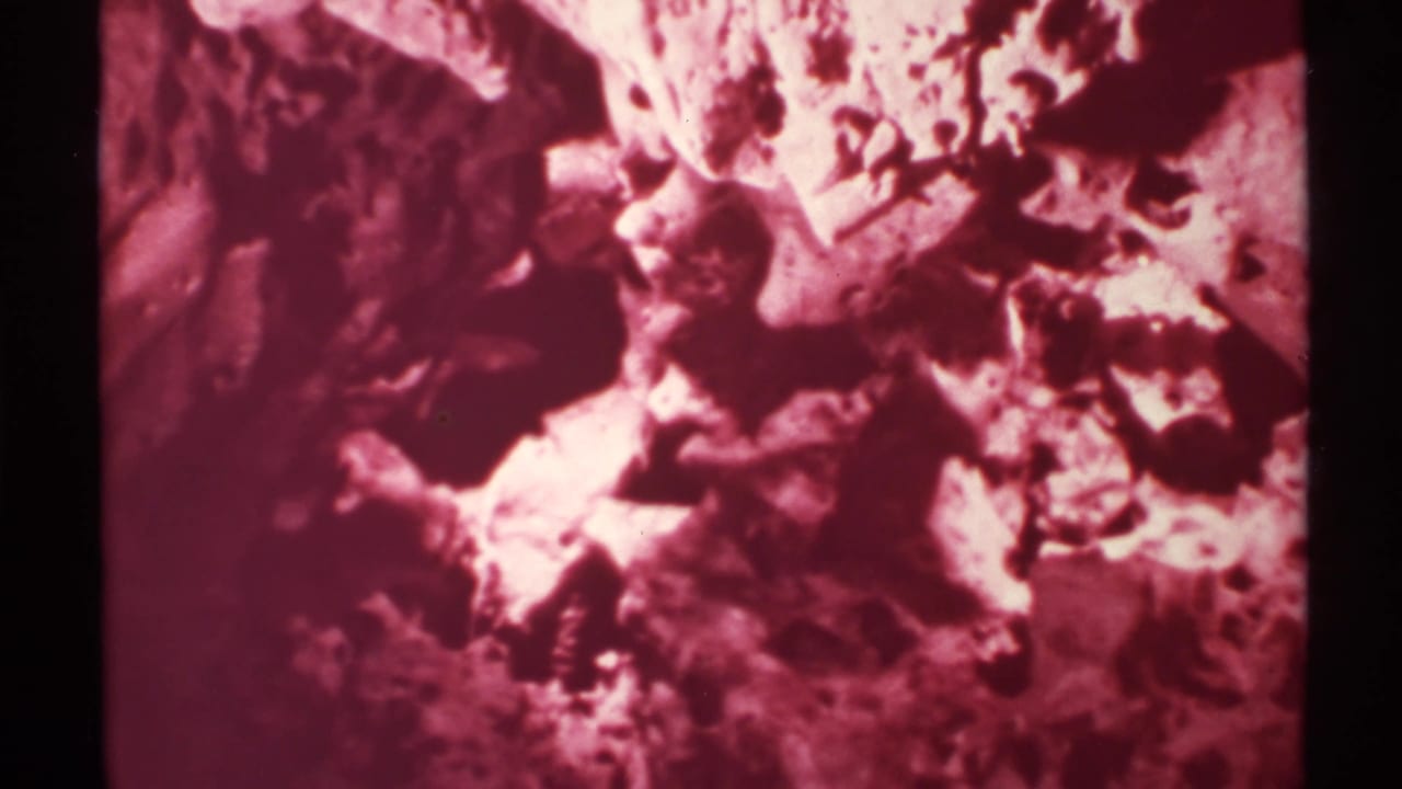 1972 8mm frame of a red-tinted cave interior in New Mexico, with rough rock surfaces and dark recesses.