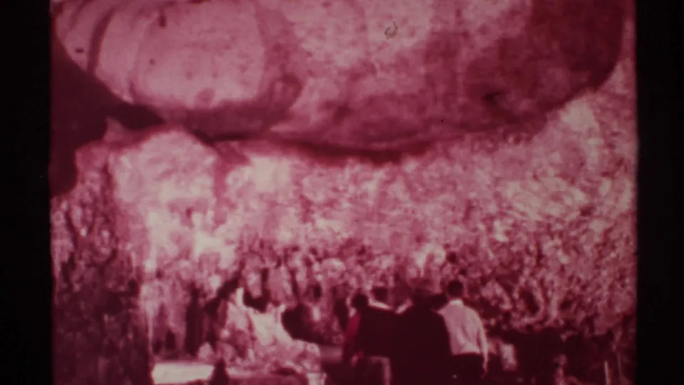 1972 New Mexico 8mm frame of several adults in formal attire moving through a cave under textured rock formations.