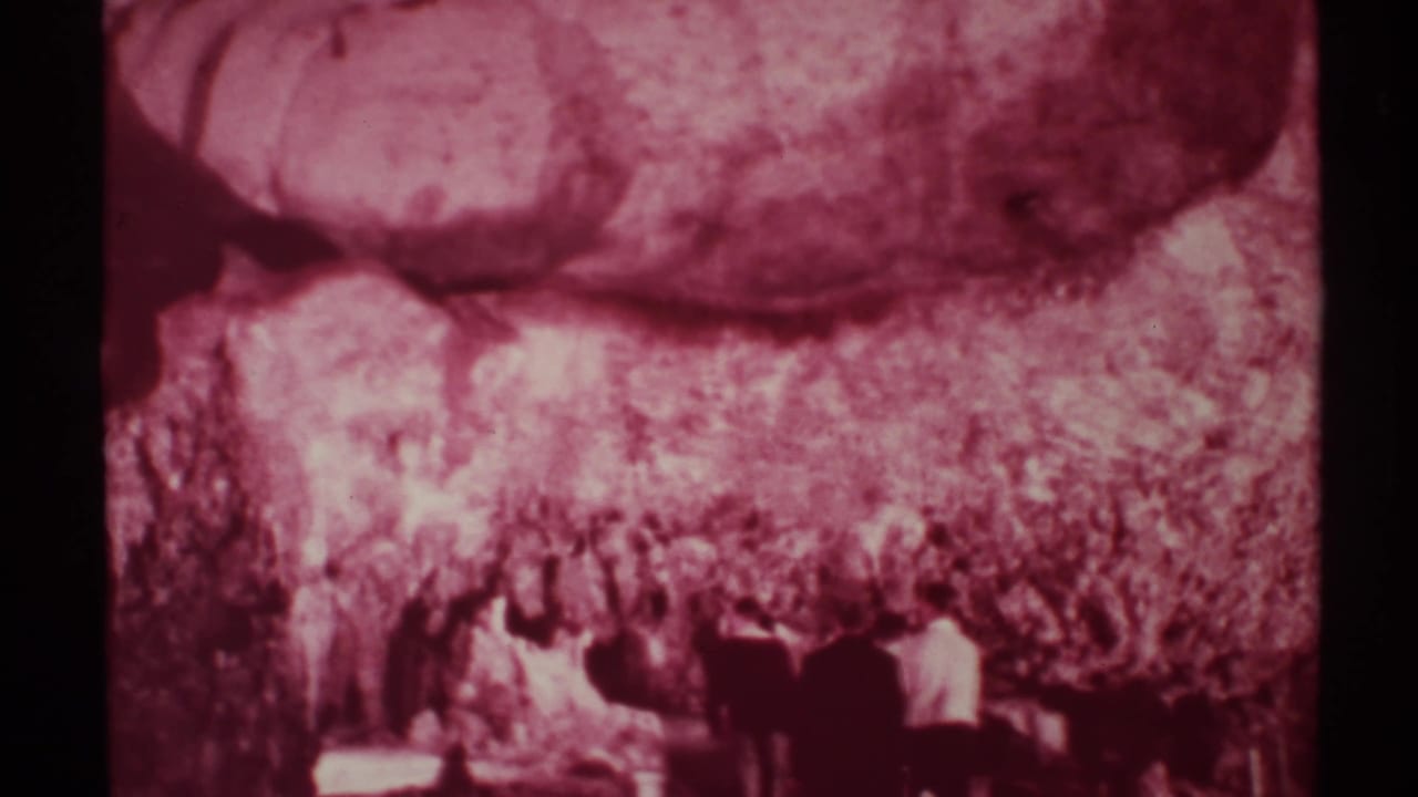 1972 New Mexico 8mm frame showing visitors moving through a dark cave area under broad, rough rock formations.