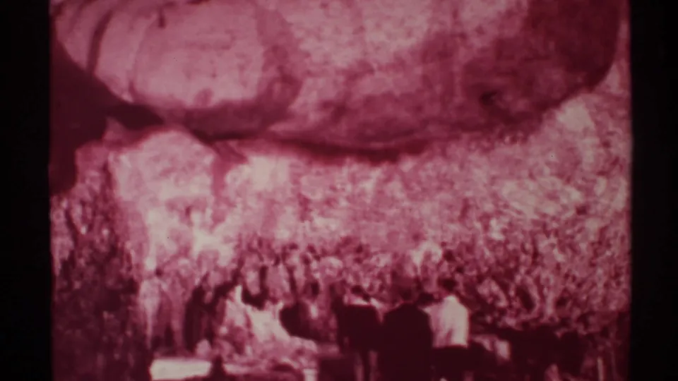 1972 New Mexico 8mm frame showing visitors moving through a dark cave area under broad, rough rock formations.