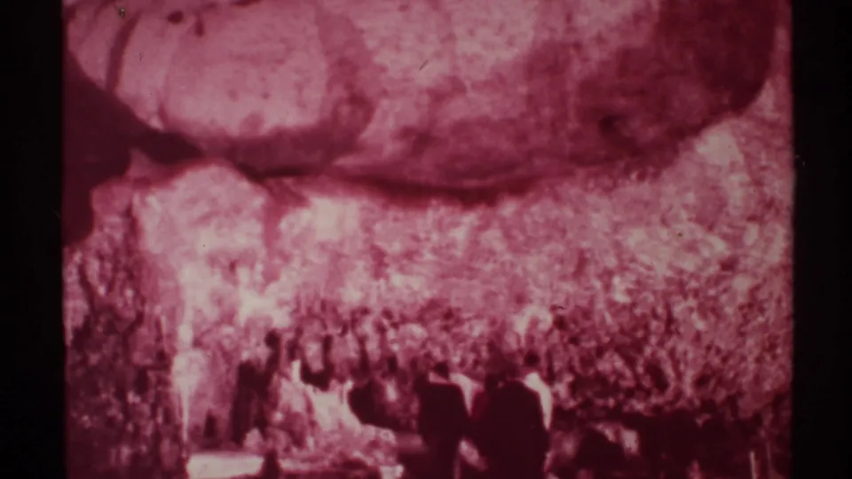 1972 New Mexico home-movie frame of several visitors inside a maroon-tinted cavern, seen from a distant handheld viewpoint.