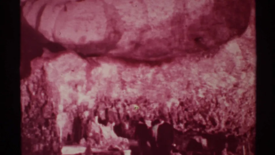 1972 New Mexico 8mm frame showing a broad cavern surface above a dark lower area with distant visitors.