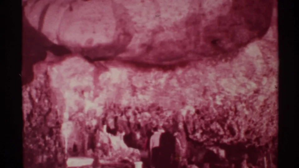 1972 New Mexico 8mm frame showing hikers as dark silhouettes beneath a magenta-shifted rocky canyon wall.