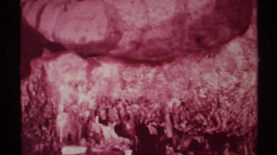 1972 home-movie frame of hikers partly obscured by darkness and grain in a rocky New Mexico canyon.