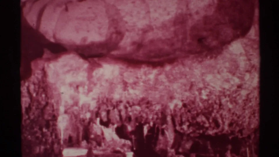 1972 New Mexico 8mm frame showing a dim cave wall and formations with visitors silhouetted near the bottom.