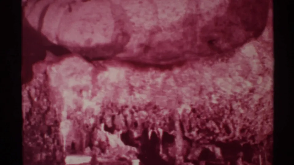 1972 New Mexico cave-tour frame with rocky formations, low light, and small silhouetted visitors in the foreground.