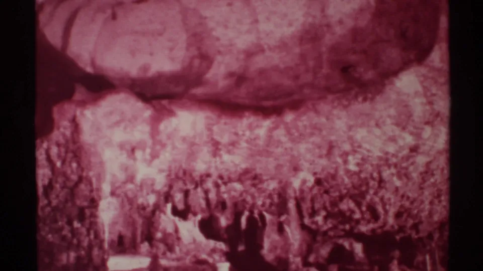 Magenta-shifted 1972 New Mexico home-movie frame of cave formations with visitors partially visible at the bottom.