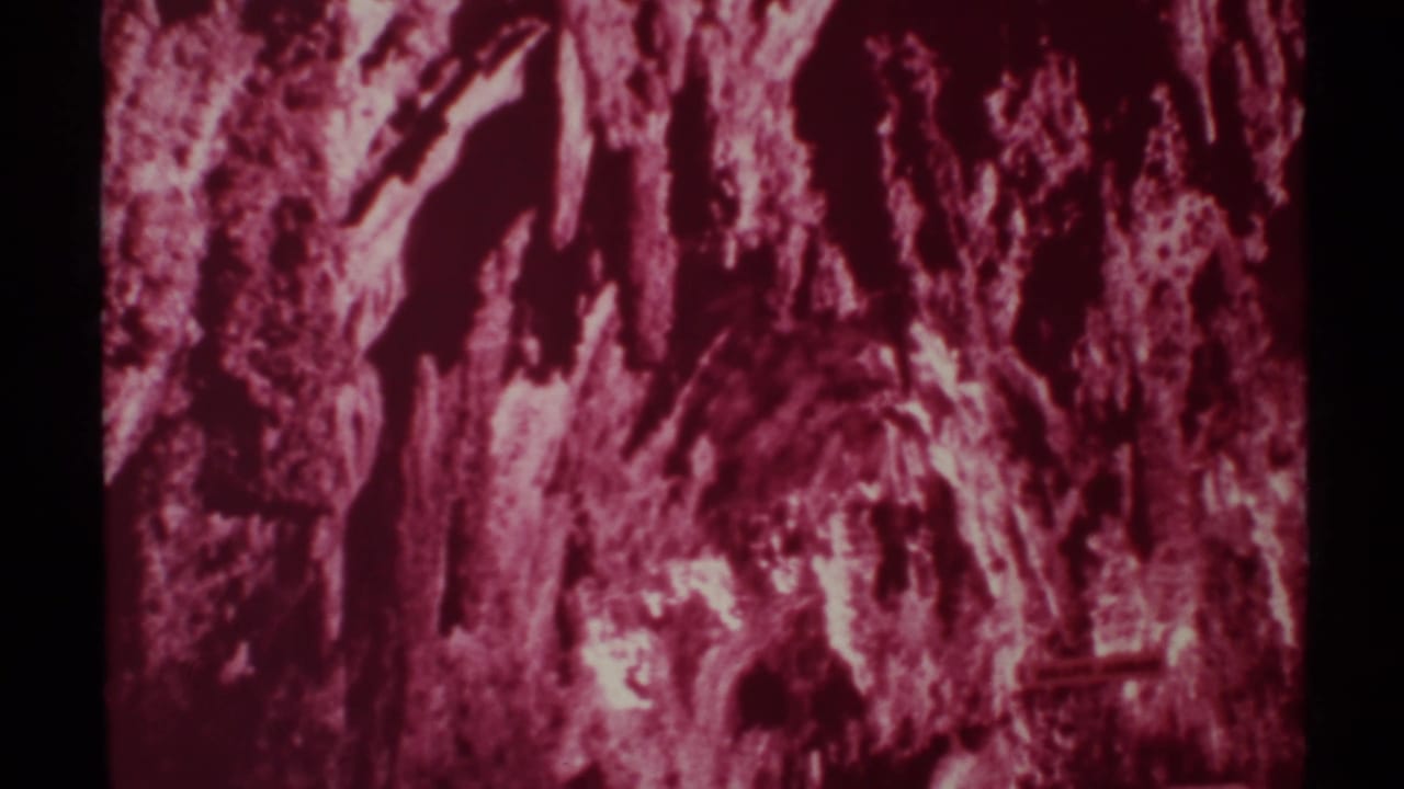 Pink-red cave wall with rough protruding rock textures and dark film borders.