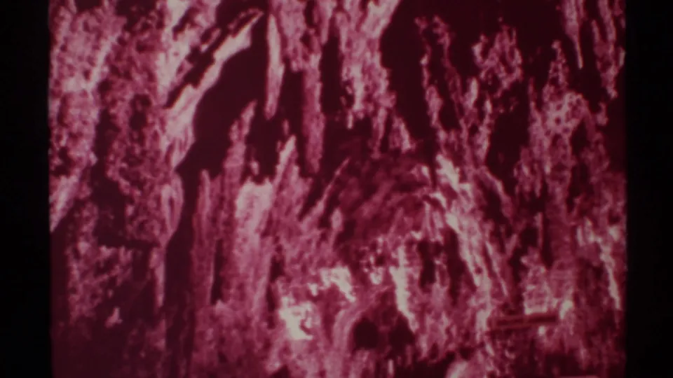 1972 8mm New Mexico cave interior showing saturated pink-red rock formations, rough wall texture, and deep shadowed recesses.