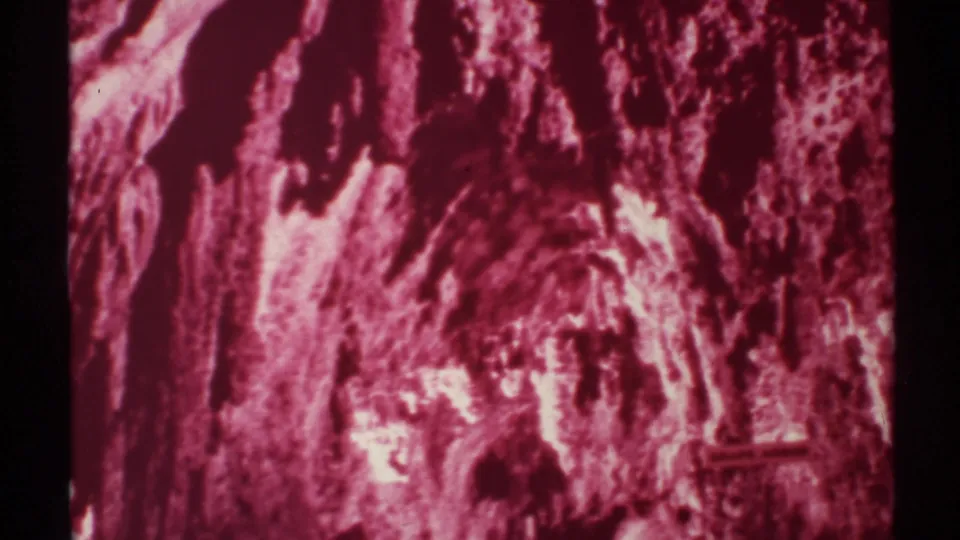 1972 8mm New Mexico cave detail showing layered mineral surfaces, saturated red-pink exposure, and dark irregular openings in the rock.