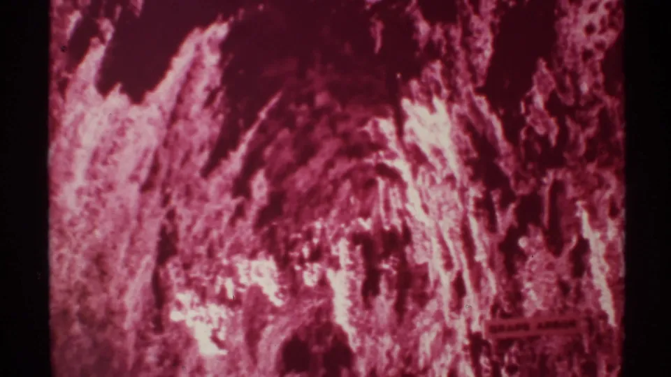 1972 New Mexico 8mm frame of a dim cave passage, red cast across rough stone, with a readable Grape Arbor sign on the right.