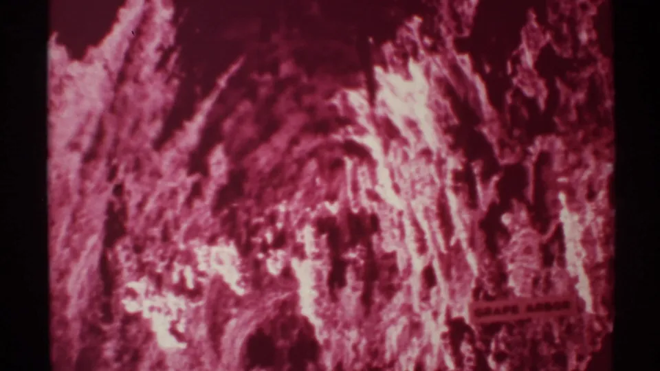 1972 New Mexico 8mm frame holding on red-lit cavern textures, deep shadowed recesses, and the Grape Arbor sign near the bottom right.