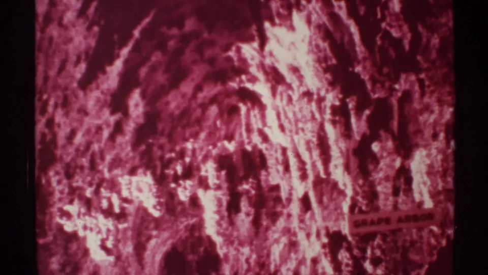 1972 New Mexico 8mm frame of a static red-magenta cave view, with rough formations and the Grape Arbor sign visible at lower right.
