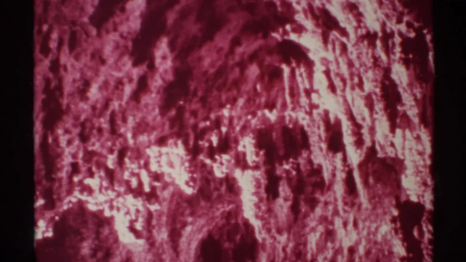 Magenta 8mm frame of a New Mexico cave wall, with a small sign reading GRAPE ARROW partly visible at the right.