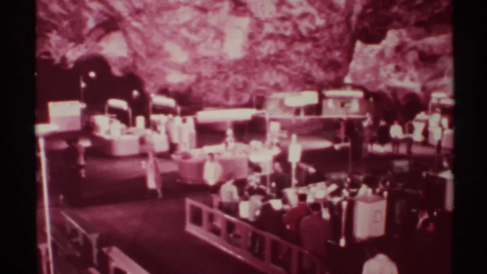 New Mexico cave exhibit area in 1972 home-movie footage, showing tables, artificial lights, and visitors under a rock wall.