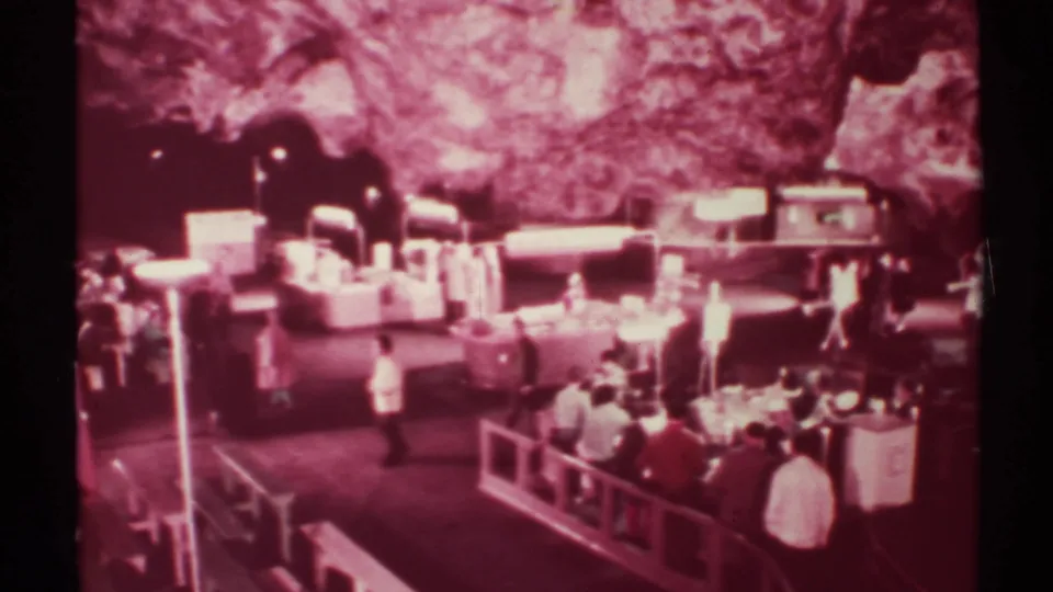 1972 New Mexico 8mm frame of visitors waiting and watching displays beneath a rocky cavern ceiling and bright exhibit lights.