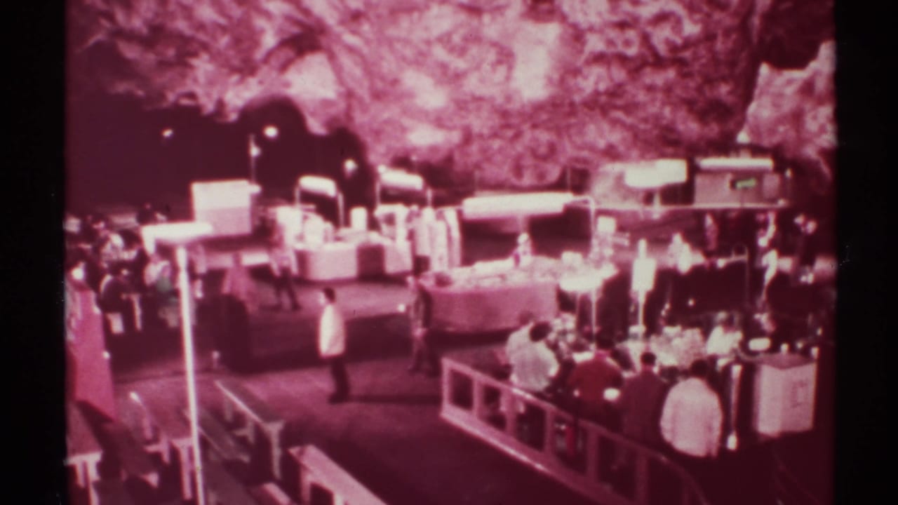 1972 8mm frame of visitors near display counters in a rock-walled indoor market setting in New Mexico.