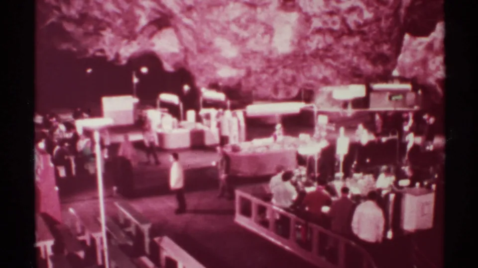 1972 8mm frame of visitors near display counters in a rock-walled indoor market setting in New Mexico.