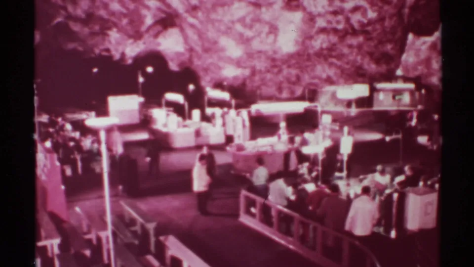 1972 home-movie frame showing a busy cave-market scene with visitors clustered around counters and railings.