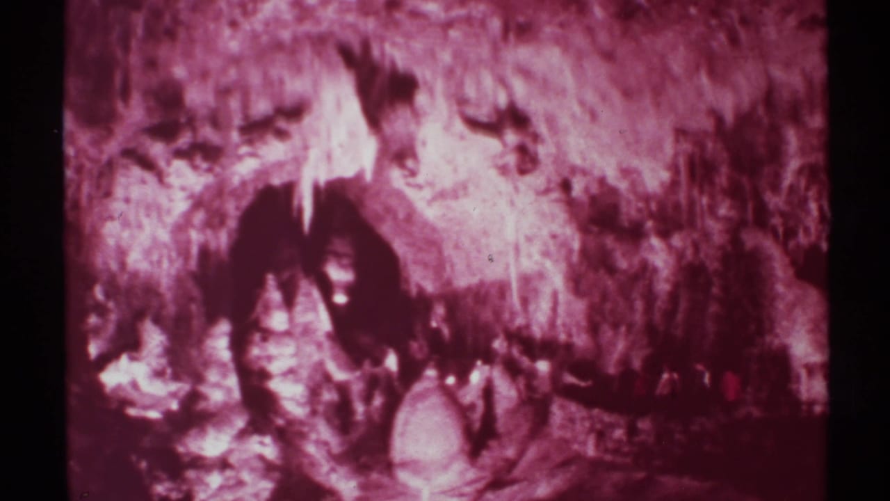 1972 8mm frame of visitors moving through a dim cavern passage in New Mexico, with stalactite-like formations and heavy magenta film aging.