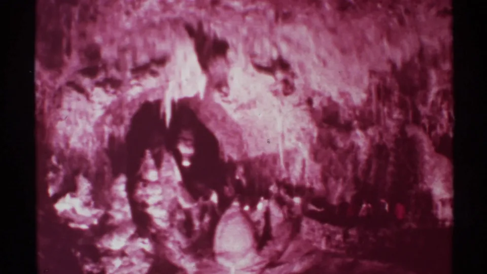 1972 8mm frame of visitors moving through a dim cavern passage in New Mexico, with stalactite-like formations and heavy magenta film aging.