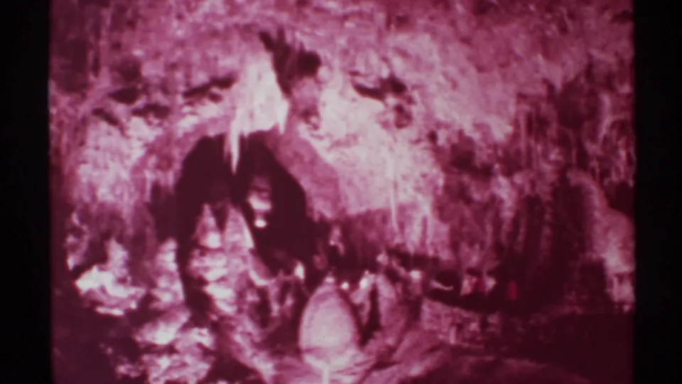 1972 home-movie frame showing visitors in a New Mexico cavern, mostly in shadow beside rough walls and bright mineral formations.