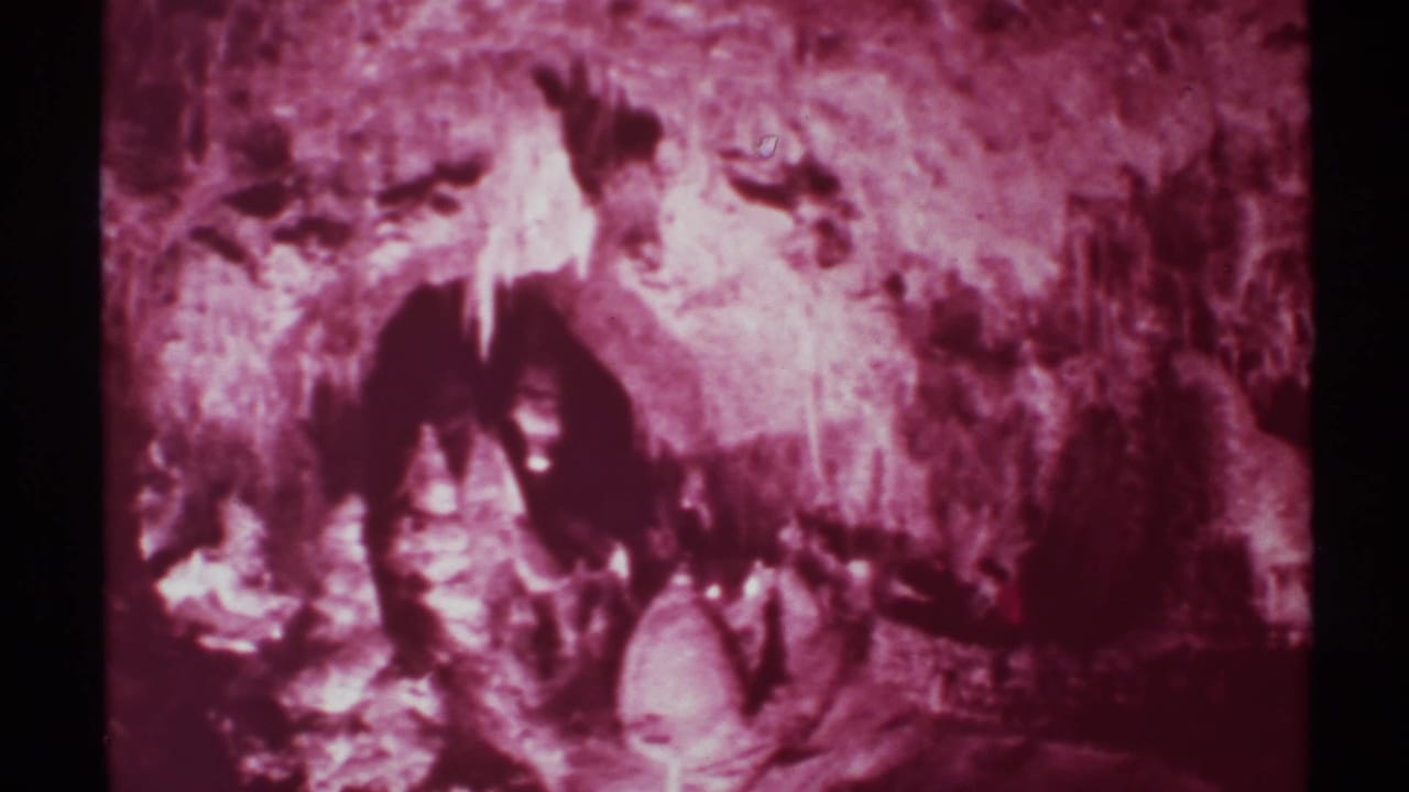 1972 New Mexico home-movie frame showing visitors silhouetted inside a cave with textured rock walls and hanging formations.