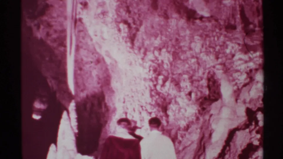 1972 New Mexico cave footage shows visitors from behind beside a bright cave light and rough mineral formations.
