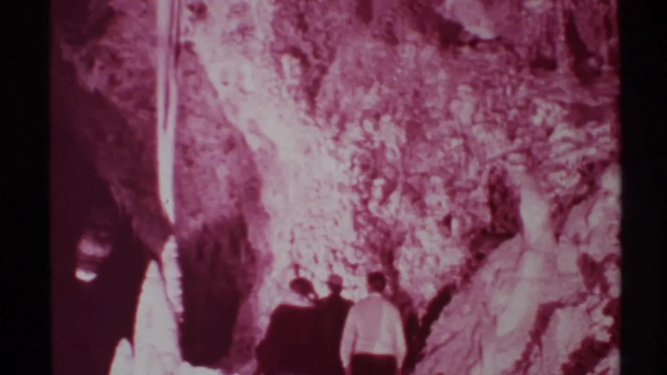 1972 New Mexico Super 8 frame showing several cave visitors near illuminated rock formations with heavy magenta film fading.