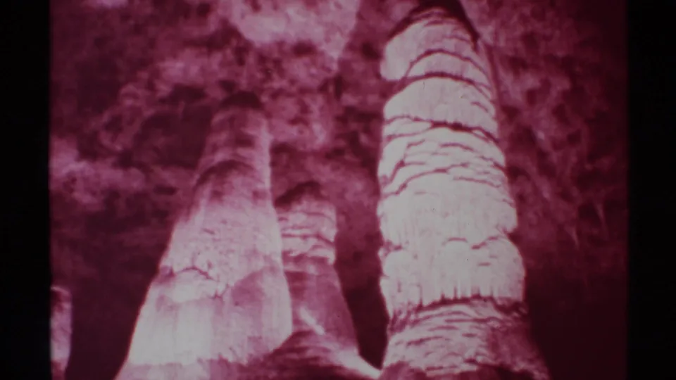 Maroon-tinted 8mm view of tall cave formations in New Mexico, with rough stone texture and no clear people in this frame.