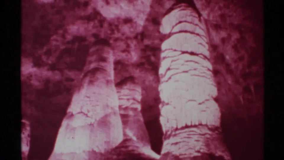 1972 New Mexico cave view with two prominent layered formations, rough walls, and aged magenta 8mm film texture.